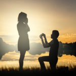 Wedding proposal concept. Young couple have dating at sun set. Man in love is kneeling on knees and giving wedding ring to surprised woman.